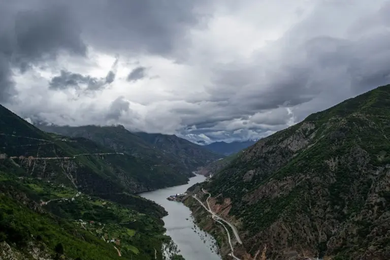 A river winding between steep green valley walls under a heavy, dark sky