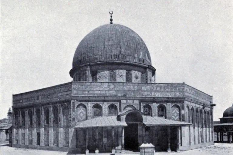 A black-and-white photograph of the Dome of the Rock in Jerusalem: a ribbed dome on a drum above an eight-sided tiled building, with a roofed porch at the front