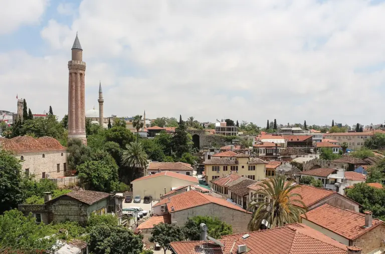 A tall brick minaret with eight vertical flutes and a blue cone, rising over the red-tiled roofs and the trees of Kaleiçi, the old town of Antalya