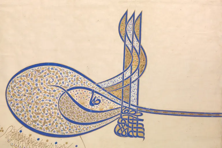 Photograph of the tughra of Süleyman the Magnificent on paper: three tall staffs, two large ovals filled with gold and blue flowers, a long band to the right and a block of stacked letters