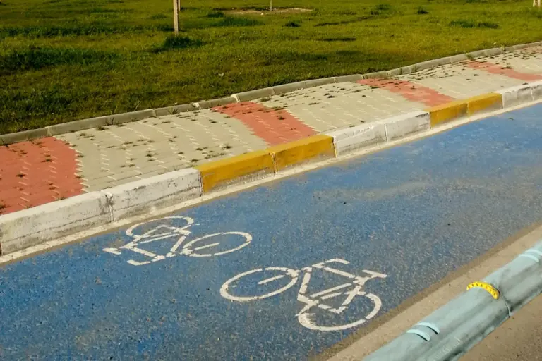 A blue cycle lane with two white bicycle signs painted on it, beside a kerb with red and yellow paving and a grass verge
