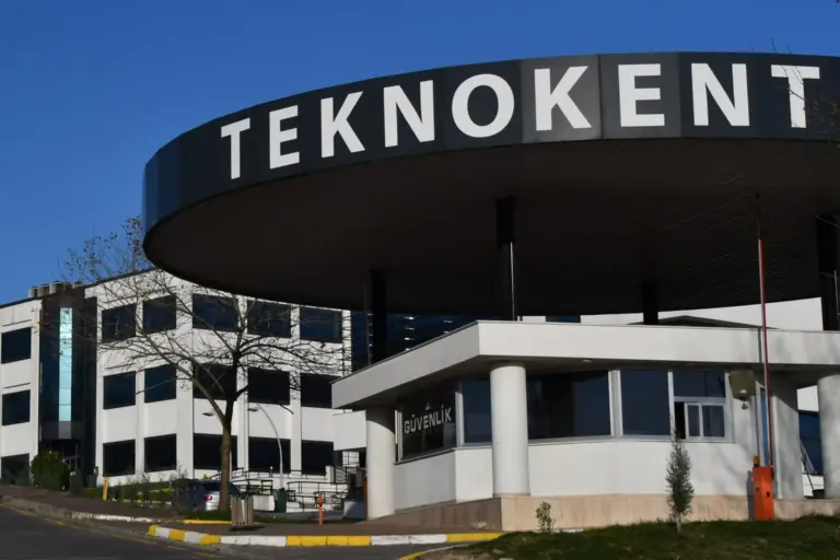 The gate of a technology development zone in Sakarya: a round dark roof with the word TEKNOKENT over a guard house, and white office buildings behind it