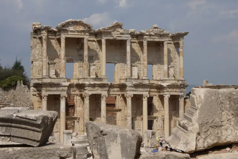 The two-storey front of the Library of Celsus at Ephesus, with columns, niches and carved stone, seen between fallen blocks of stone, with a few tiny visitors at its foot