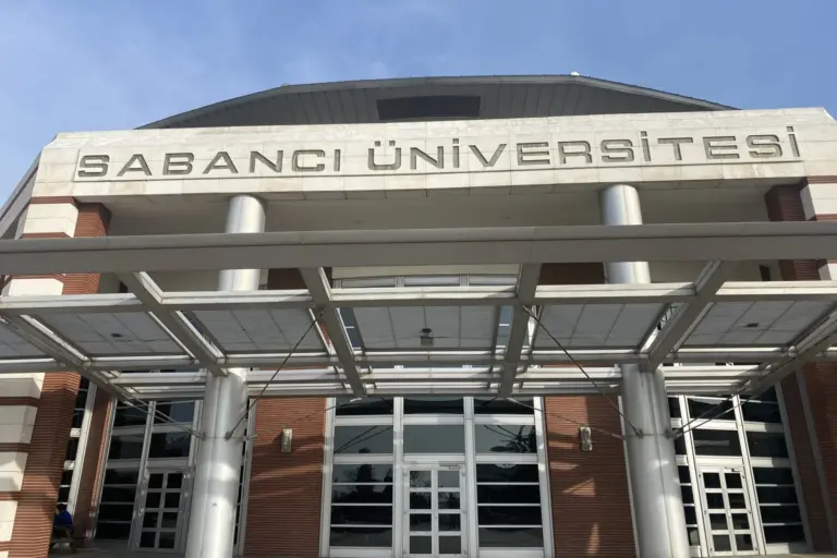 The main entrance of Sabancı University: the name in metal letters on a pale stone band over a brick and glass front, under a steel and glass canopy