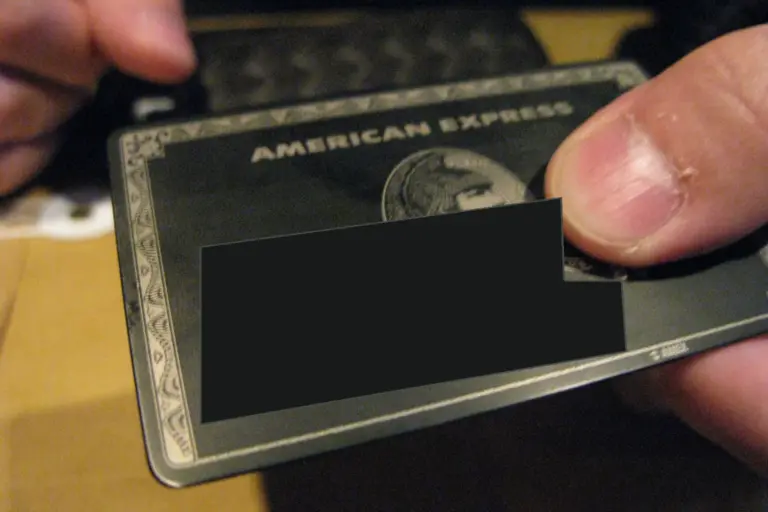A black American Express Centurion card held between two fingers, with a dark patch over the name and number