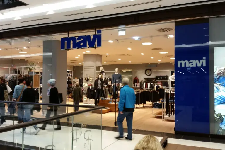 The entrance of a Mavi shop in a shopping centre, with the blue Mavi sign above racks of clothes