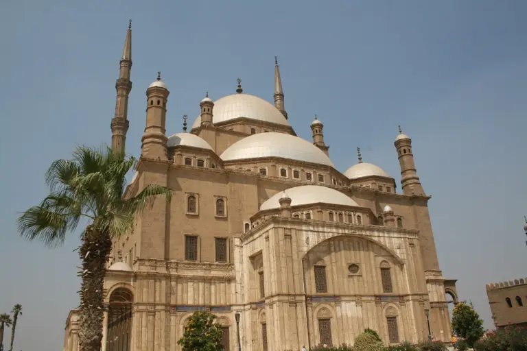 The Muhammad Ali Mosque in the Cairo Citadel: a large central dome with smaller domes round it, two tall thin minarets and palm trees in front, under a clear blue sky