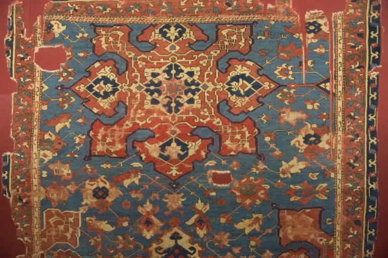 A worn old Uşak rug in blue and red: a large eight-pointed star in the middle, smaller stars and leaf shapes around it and a narrow border at the edge