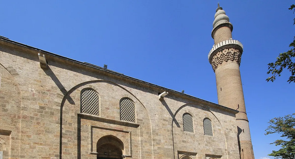 The stone wall and brick minaret of Ulu Cami in Bursa against a blue sky