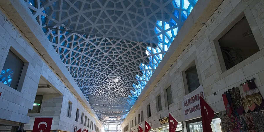 A roofed shopping street in Bursa with a white lattice vault overhead, shop fronts on both sides and red flags