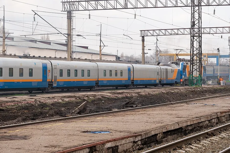A passenger train with blue and orange stripes on a track beside a bare platform, under overhead wires