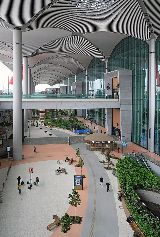 The entrance hall of Istanbul Airport with a high ribbed roof, a glass wall and people walking across a paved plaza