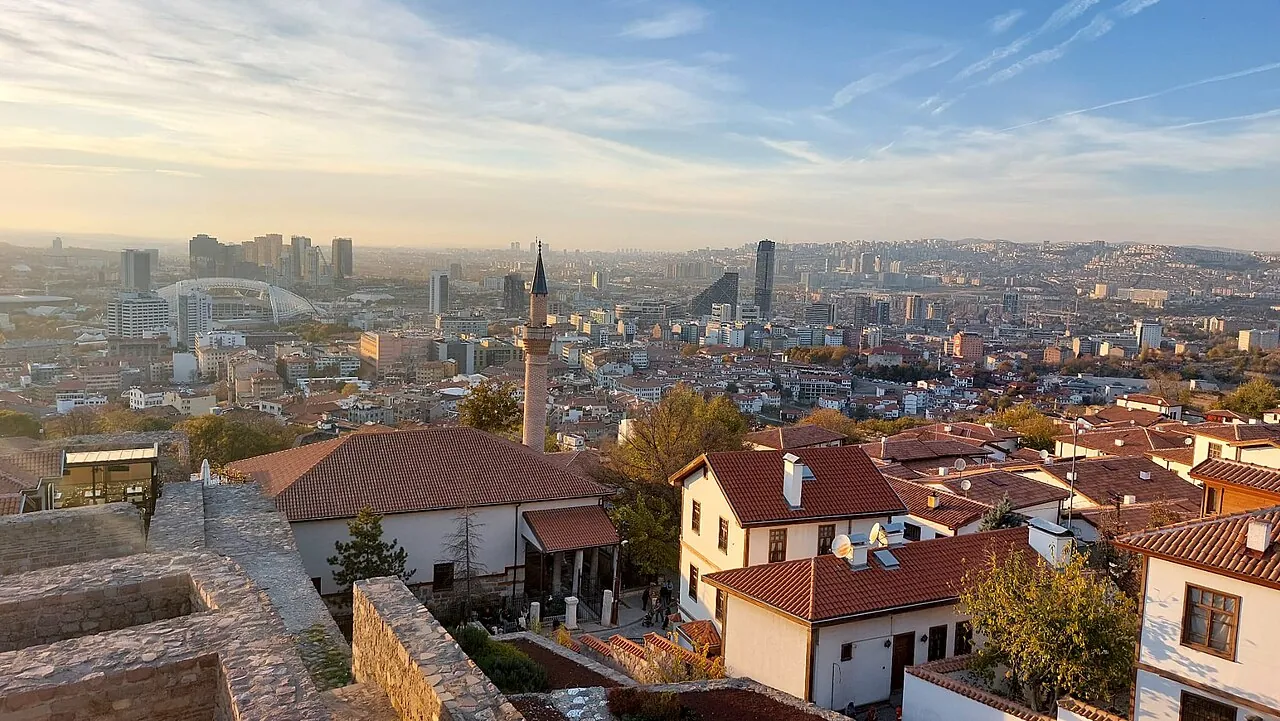 Red roofs of old houses and a minaret in the castle quarter of Ankara, with the towers of the city beyond in evening light
