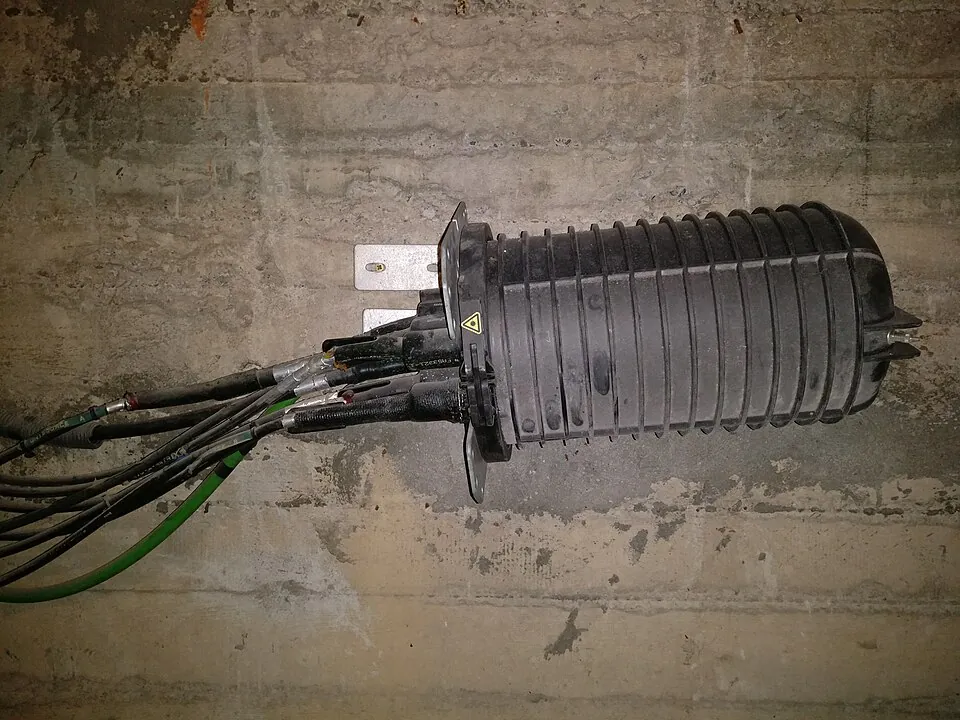 Een zwarte cilindervormige lasmof op een betonnen muur, met kabels die aan &eacute;&eacute;n kant naar binnen gaan