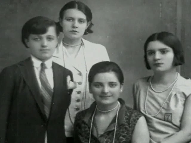 Fotografie: patru tineri pozează &icirc;mpreună &icirc;ntr-un studio; unul poartă sacou &icirc;nchis la culoare și cravată, iar ceilalți trei, bluze sau rochii cu coliere de perle