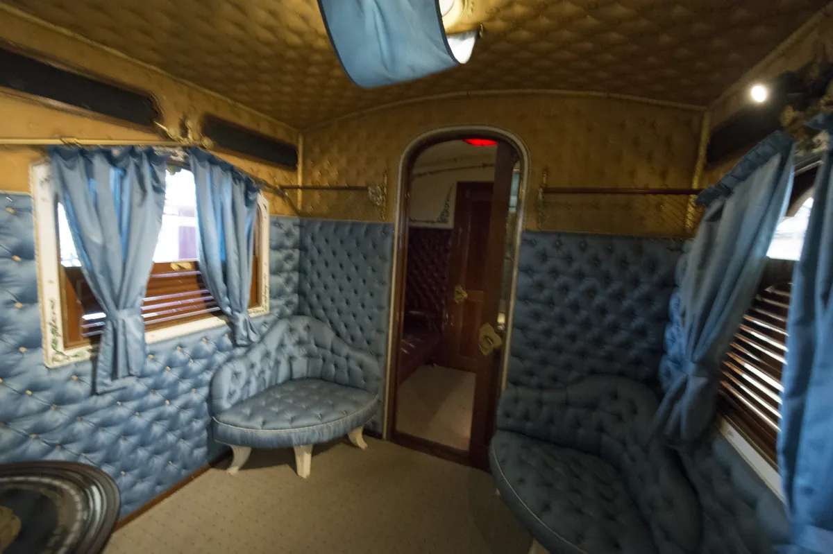 Inside a railway coach: blue tufted seats, curtained windows and a gilded padded ceiling