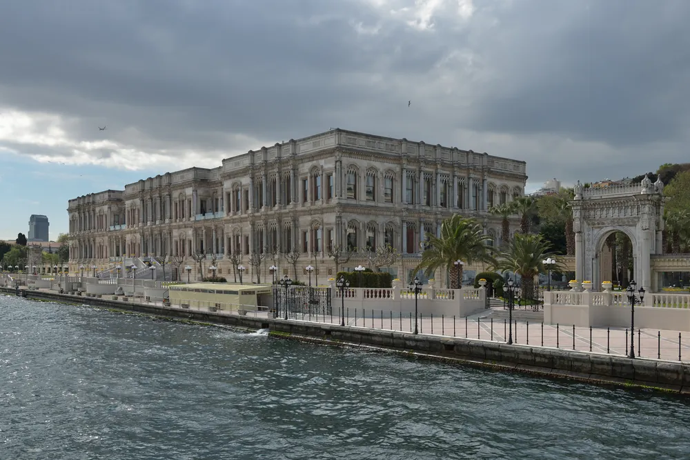 The long three-storey sea façade of Çırağan Palace beside a stone quay, with an ornate stone gate on the right