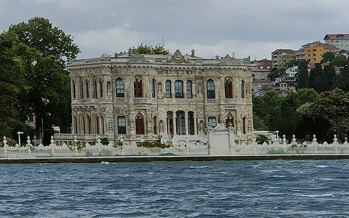 Boğaz kıyısında, arkasındaki tepede ağaçlar bulunan, çok sayıda kemerli penceresi olan küçük beyaz bir sarayın denizden görünümü