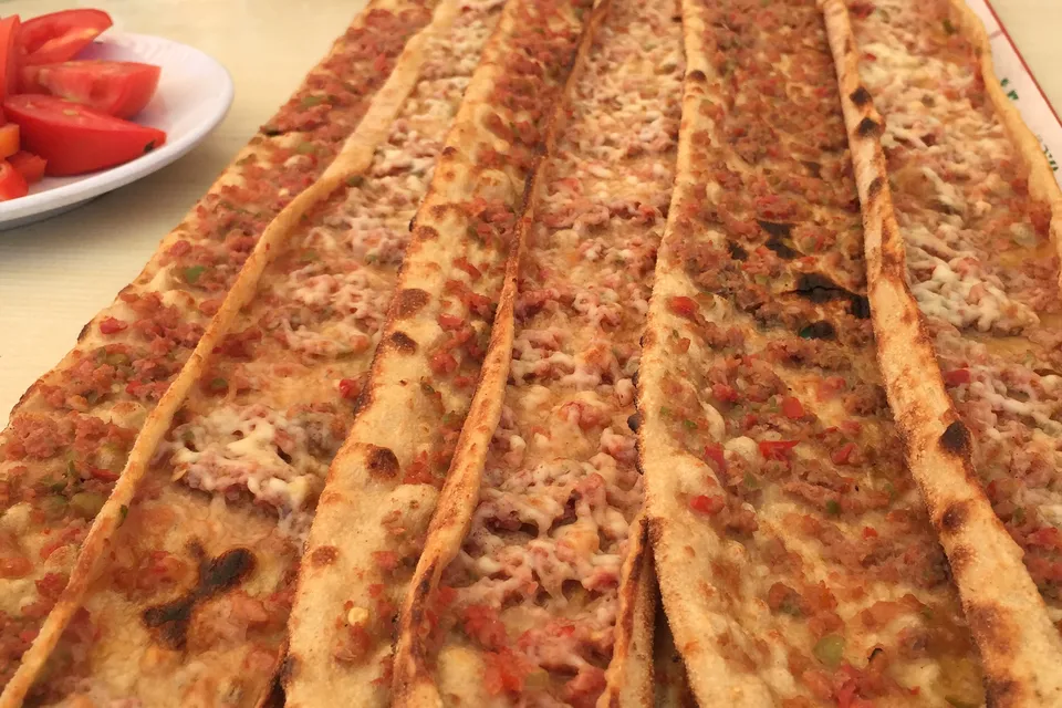 De longs pains plats garnis de viande hach&eacute;e et de fromage fondu, align&eacute;s &agrave; c&ocirc;t&eacute; d&rsquo;une assiette de rondelles de tomate