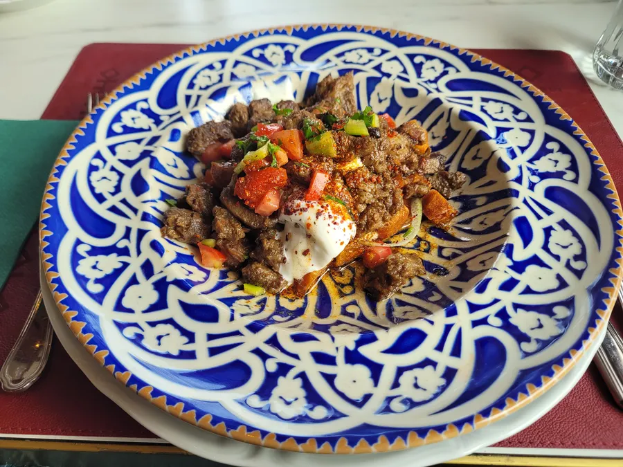 Une assiette &agrave; motifs bleus et blancs contenant des d&eacute;s de viande dor&eacute;s, surmont&eacute;s d&rsquo;une cuiller&eacute;e de yaourt, de tomate hach&eacute;e et de poivron vert