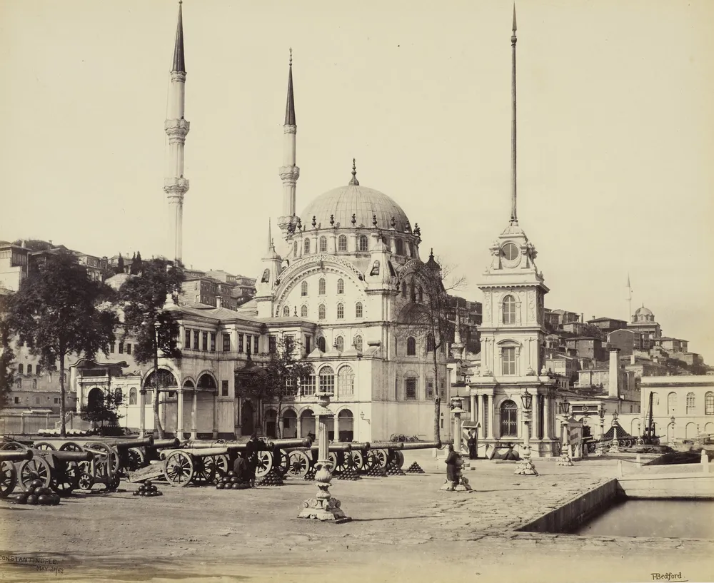 Fotograf&iacute;a de 1862: la mezquita de Nusretiye con su c&uacute;pula y dos minaretes junto a una peque&ntilde;a torre del reloj, con ca&ntilde;ones y balas de ca&ntilde;&oacute;n en la plaza de delante