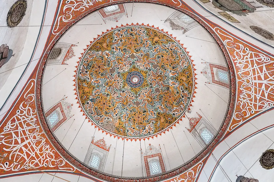 Vista de baixo de uma c&uacute;pula pintada: um medalh&atilde;o central redondo em dourado, verde e branco, cercado por caligrafia vermelha e branca e pequenas janelas