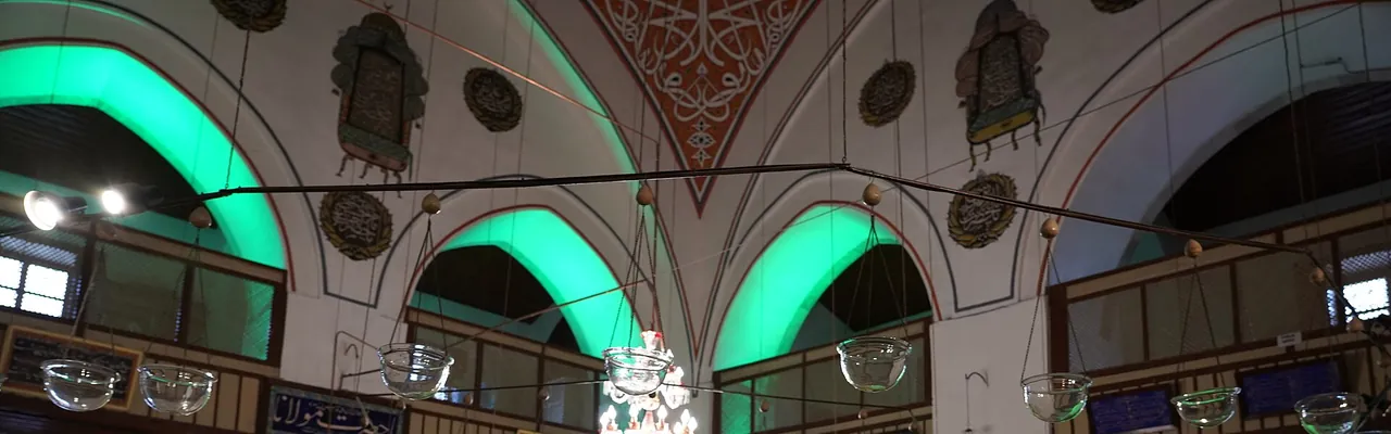A parte superior de um sal&atilde;o circular: arcos iluminados em verde, lumin&aacute;rias de vidro suspensas e um ornamento pintado no teto