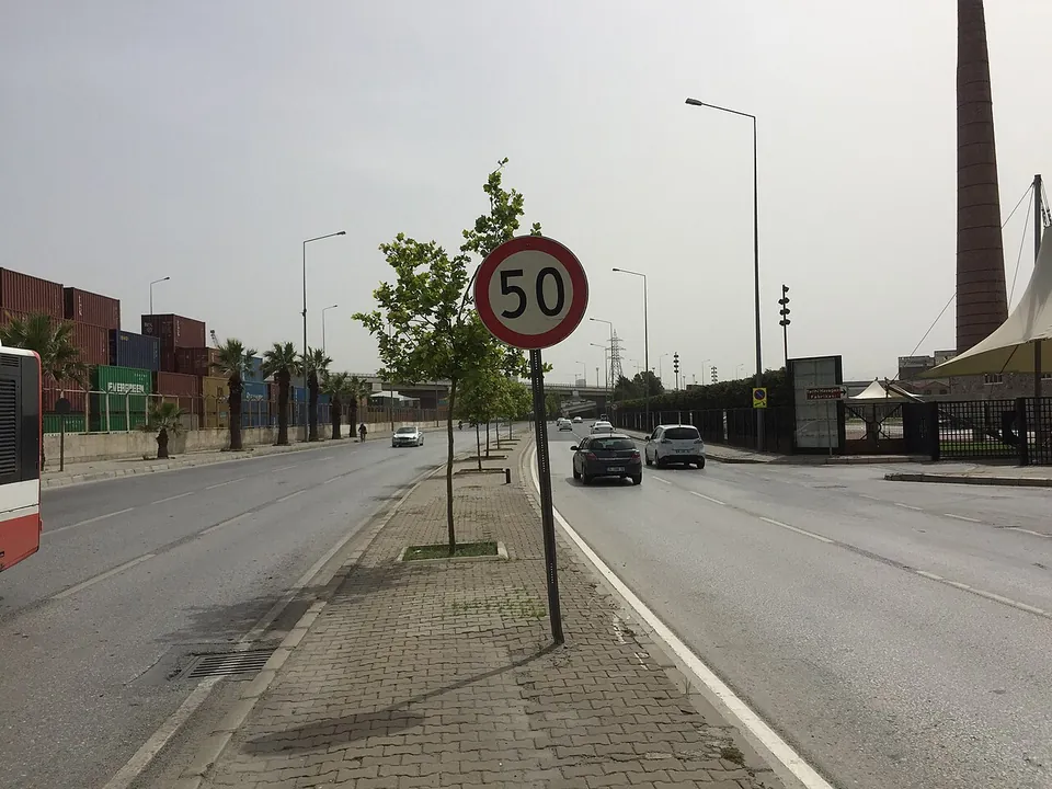 Un panneau rond limitant la vitesse à 50 km/h au bord d’une large route urbaine à İzmir, avec quelques voitures et des lampadaires