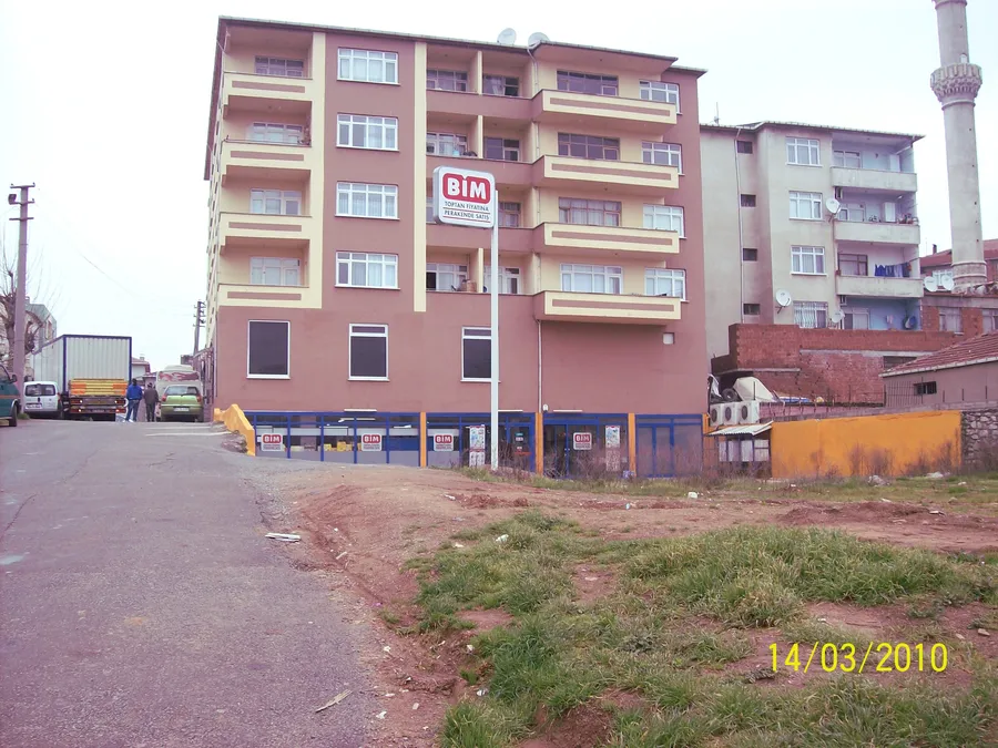 Un magasin BİM au rez-de-chauss&eacute;e d&rsquo;un immeuble d&rsquo;habitation rose au bout d&rsquo;une rue, avec une enseigne BİM sur un poteau
