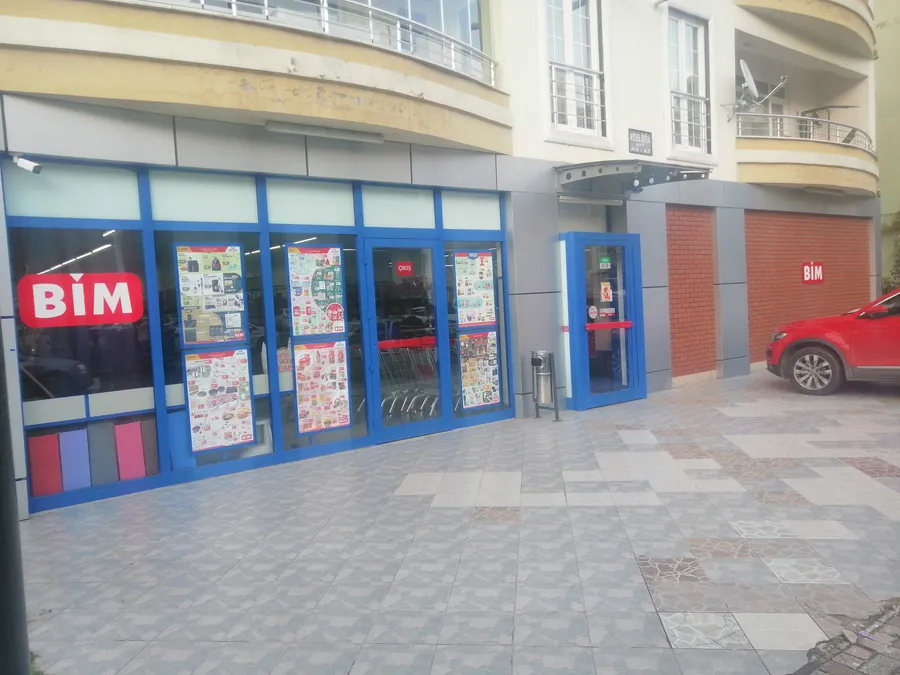 La fa&ccedil;ade d&rsquo;un magasin BİM avec des encadrements de fen&ecirc;tres bleus et des pages de prospectus Akt&uuml;el dans les vitrines