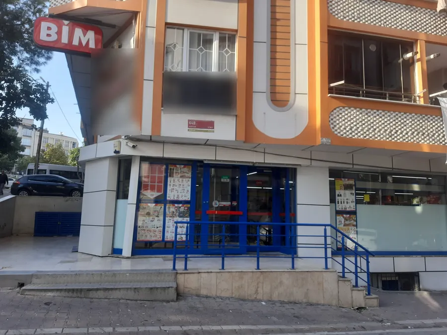 Un magasin BİM au rez-de-chauss&eacute;e d&rsquo;un immeuble d&rsquo;angle, avec une enseigne BİM au-dessus de l&rsquo;entr&eacute;e et des pages de prospectus dans la vitrine