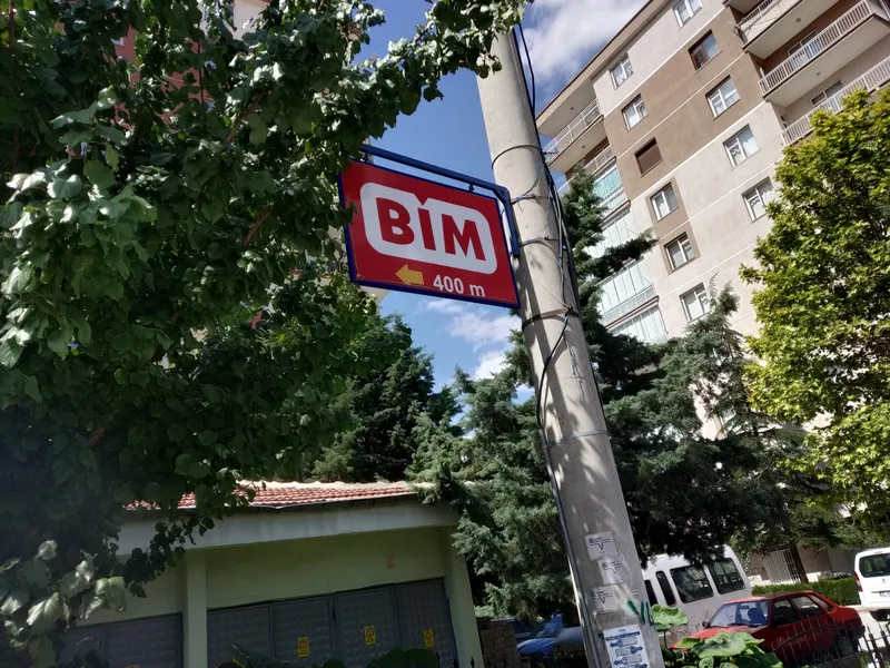 Un panneau BİM rouge avec une fl&egrave;che et l&rsquo;inscription 400 m sur un poteau entre des arbres et des immeubles d&rsquo;habitation