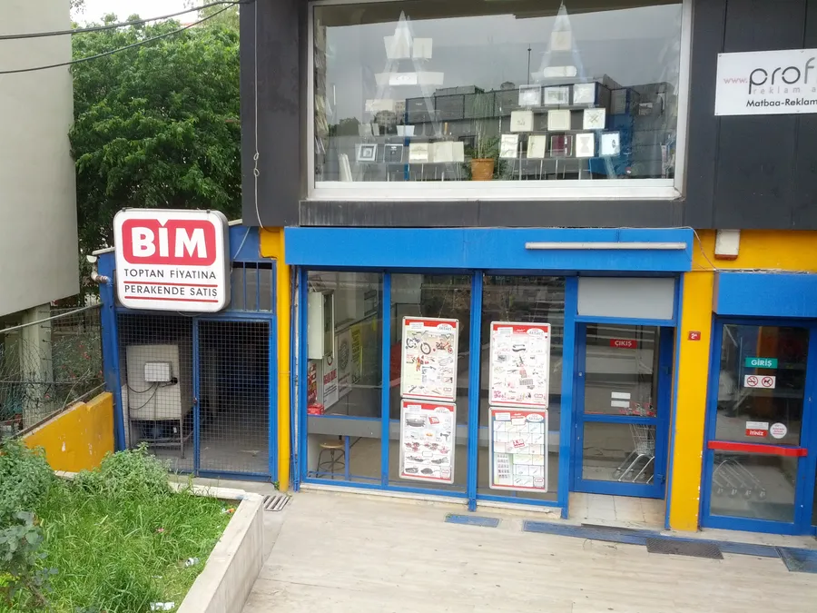 La fa&ccedil;ade d&rsquo;un magasin BİM, avec une enseigne BİM rouge et blanche, des portes vitr&eacute;es et des pages de prospectus dans les vitrines