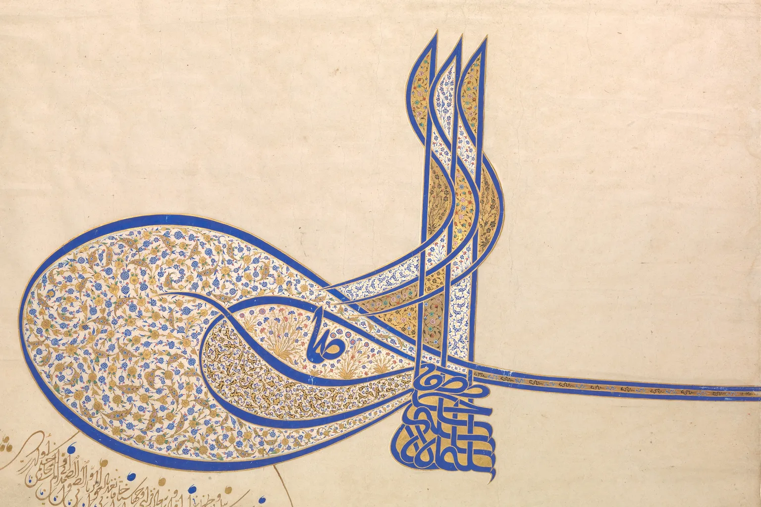 Photographie de la tugra de Soliman le Magnifique sur papier : trois hautes hampes, deux grands ovales remplis de fleurs dorées et bleues, une longue bande vers la droite et un bloc de lettres superposées
