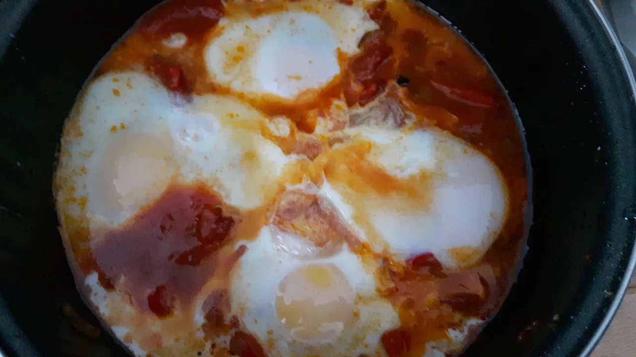 Quattro uova intere, con albumi rappresi e tuorli visibili, cotte in una salsa rossa di pomodoro in una padella nera