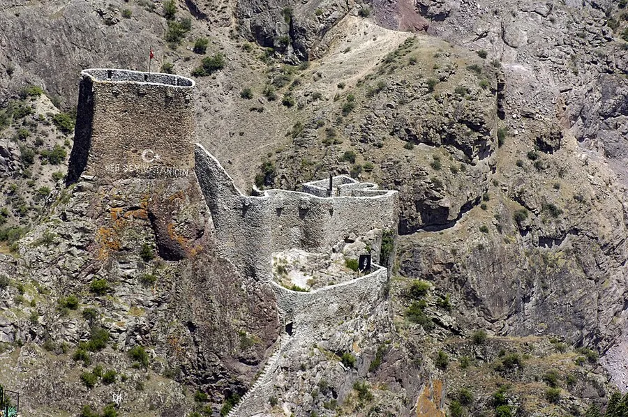 Muros de piedra de un castillo y una torre cuadrada sobre una cresta rocosa, vistos desde arriba