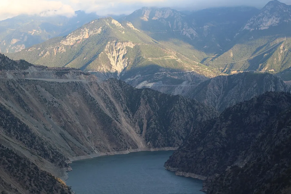 Agua gris azulada en un valle profundo entre laderas escarpadas y desnudas, con monta&ntilde;as al fondo