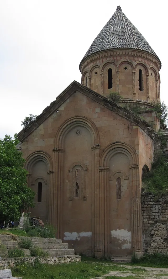 Una iglesia de piedra marr&oacute;n con tambor circular y tejado c&oacute;nico, con hornacinas en arco en los muros