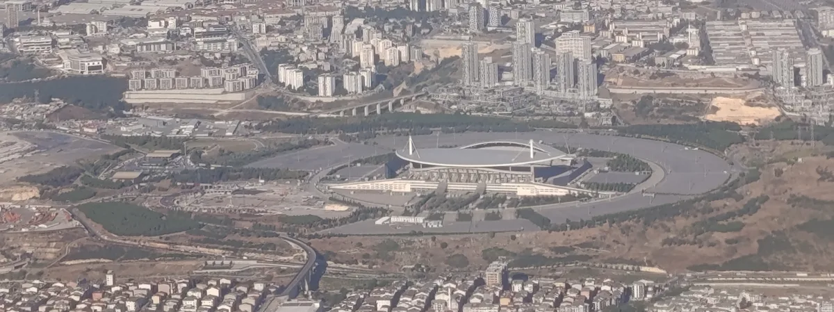 Une vue aérienne brumeuse d’un stade ovale à l’intérieur d’une route circulaire, entouré d’immeubles et de terrains dégagés