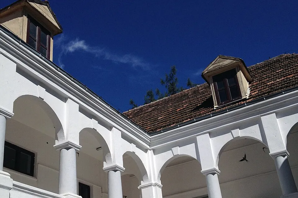 Um p&aacute;tio escolar branco com arcadas em dois lados e telhado de telhas sob um c&eacute;u azul intenso