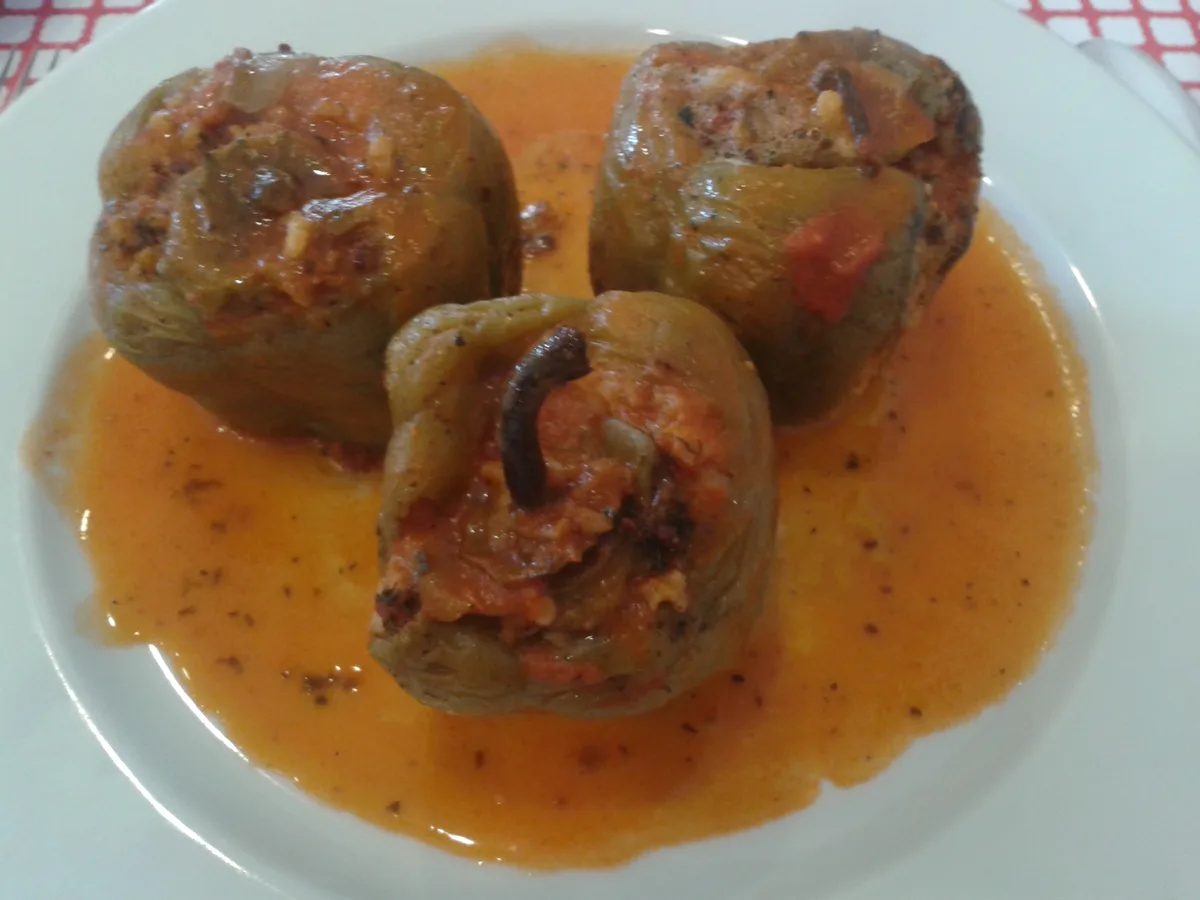 Beyaz bir tabakta, turuncu sos içinde üç biber dolması