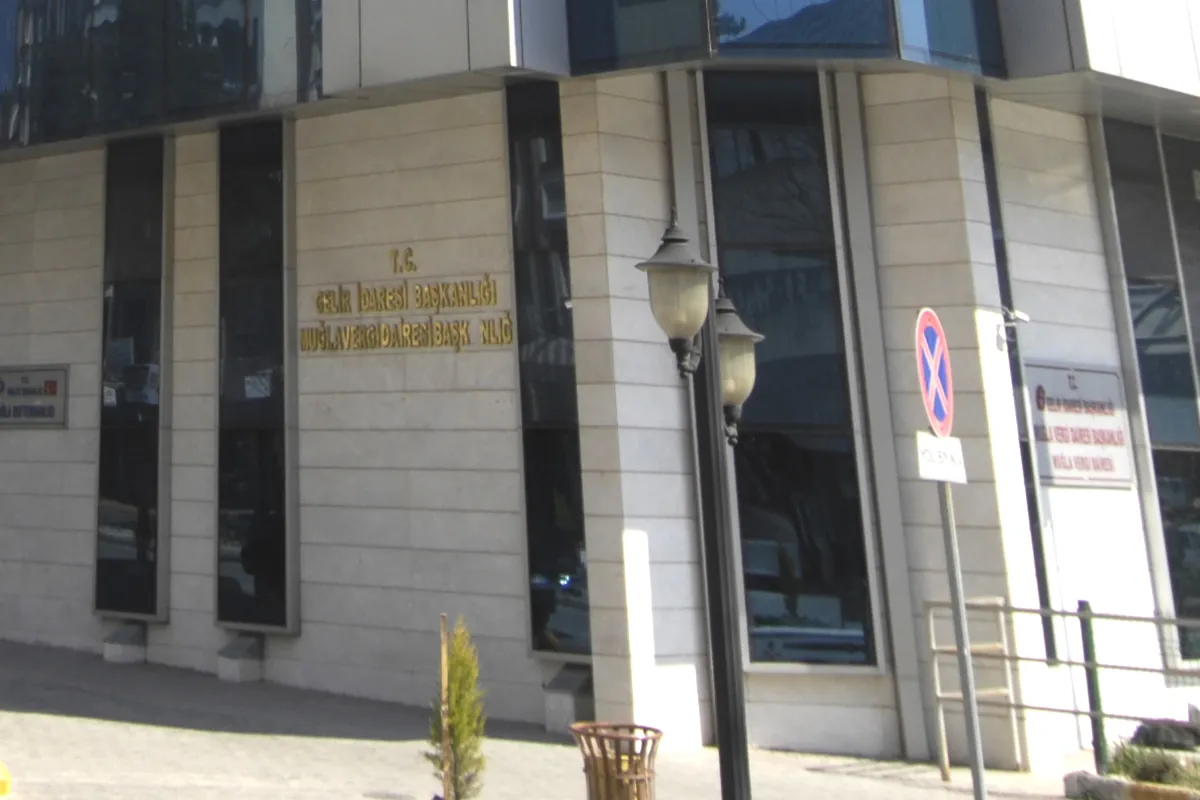 Des lettres dorées sur un mur en pierre forment l’inscription Gelir İdaresi Başkanlığı, Muğla Vergi Dairesi Başkanlığı, à côté d’un lampadaire.