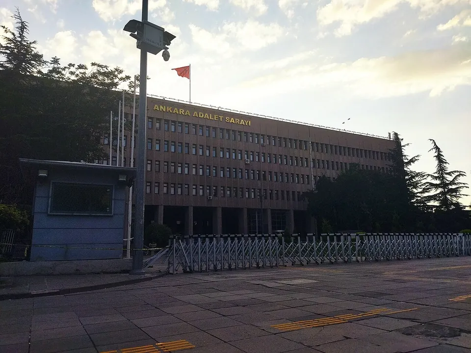 Un long palais de justice brun de l’autre côté d’un parvis vide au crépuscule, avec un drapeau turc sur son toit