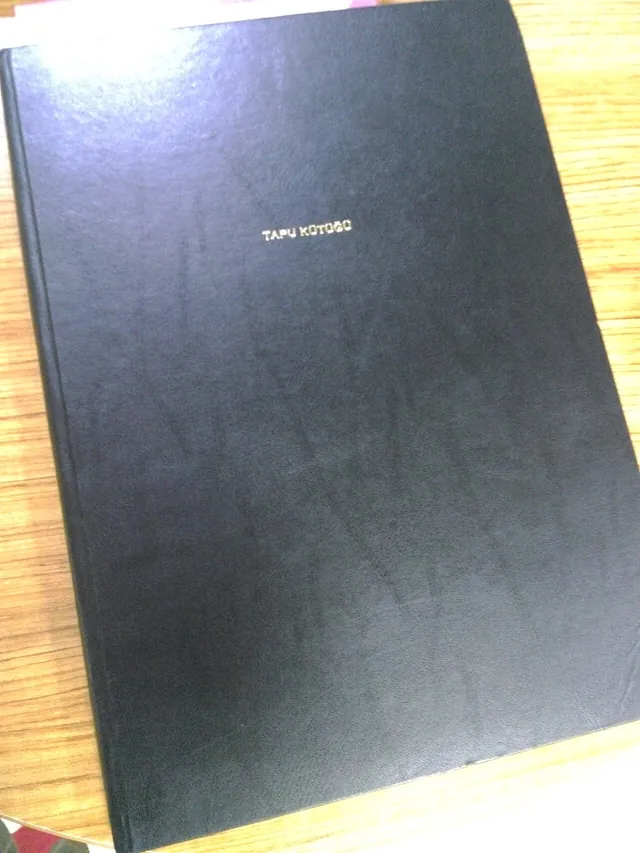 La couverture noire d’un registre relié portant de petites inscriptions, posé sur un bureau en bois