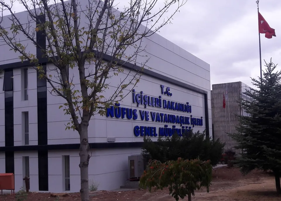 Un bâtiment administratif blanc avec une inscription bleue indiquant la direction de l’état civil et de la citoyenneté, un drapeau turc et des arbres dénudés