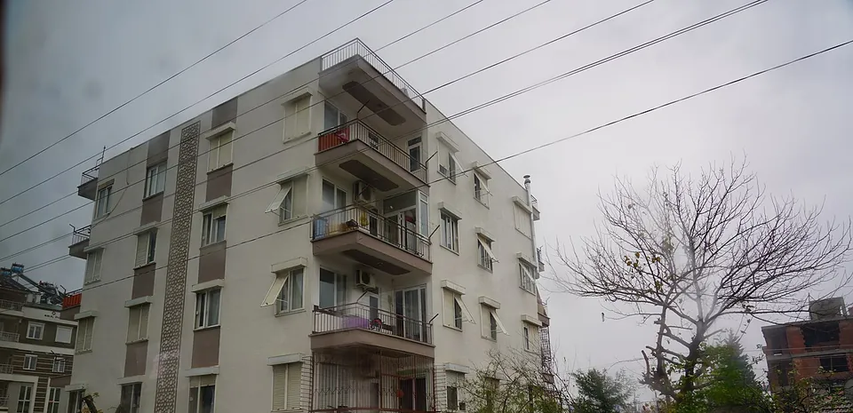 Un immeuble avec des balcons au bord d’une rue d’Antalya par temps gris, avec des lignes électriques et un arbre dénudé