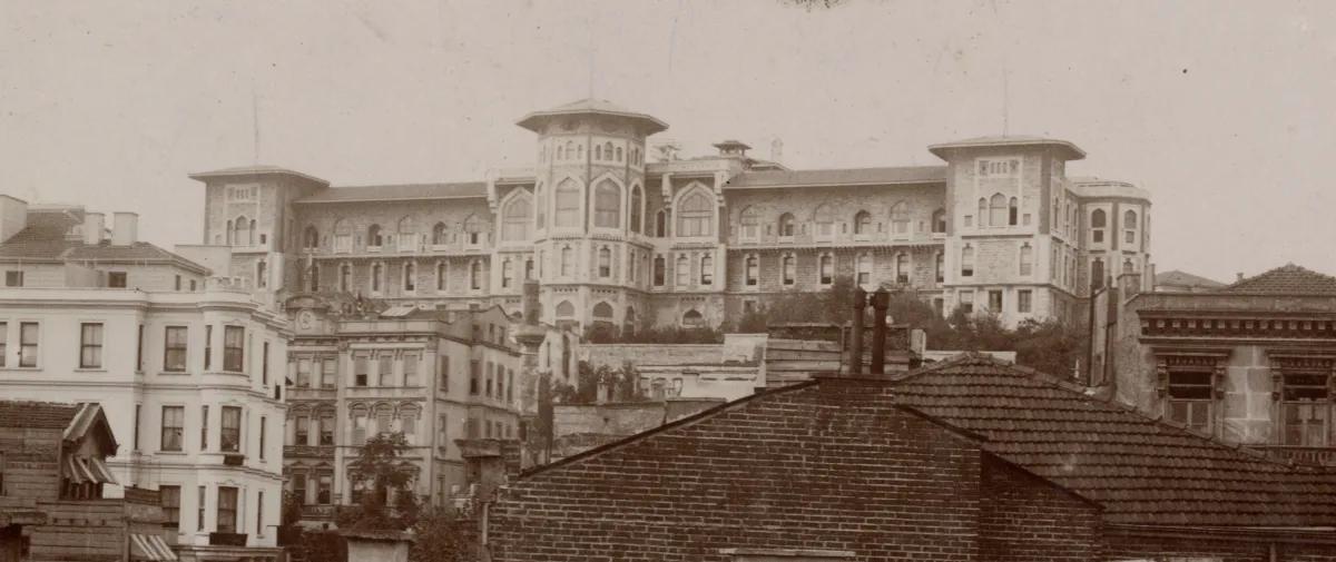 Sepia photograph of the Public Debt Administration building in Cağaloğlu: a long stone building with arched windows, a central tower with a pointed cap and corner towers, seen over brick and tile rooftops