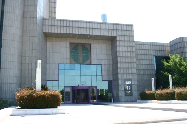 The entrance of the İstanbul Stock Exchange building: grey granite blocks, a round teal emblem over a glass doorway and a sign with the exchange&rsquo;s name