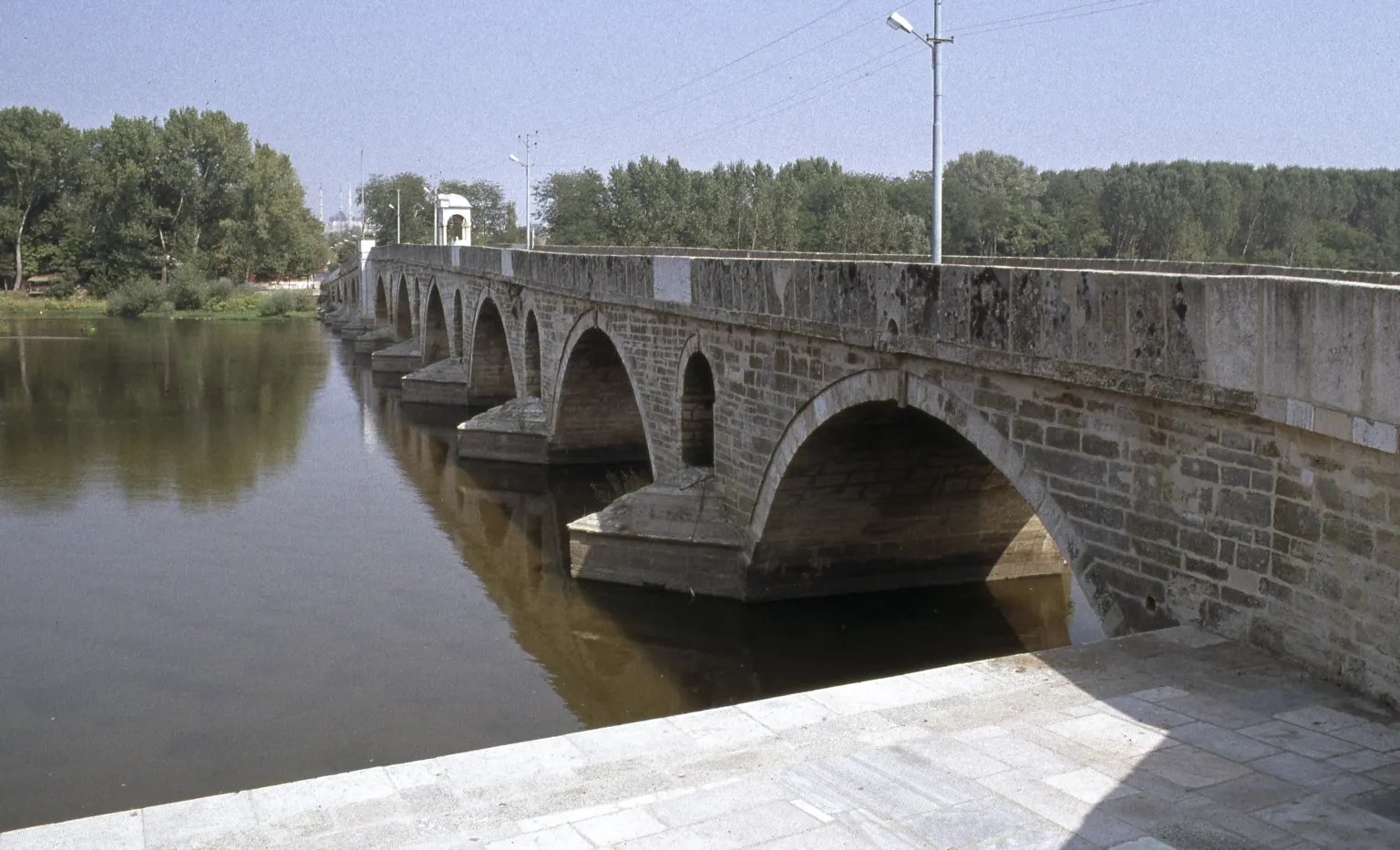 Un pont de pierre menant à une petite île boisée dans un fleuve, avec un second pont à l’arrière-plan