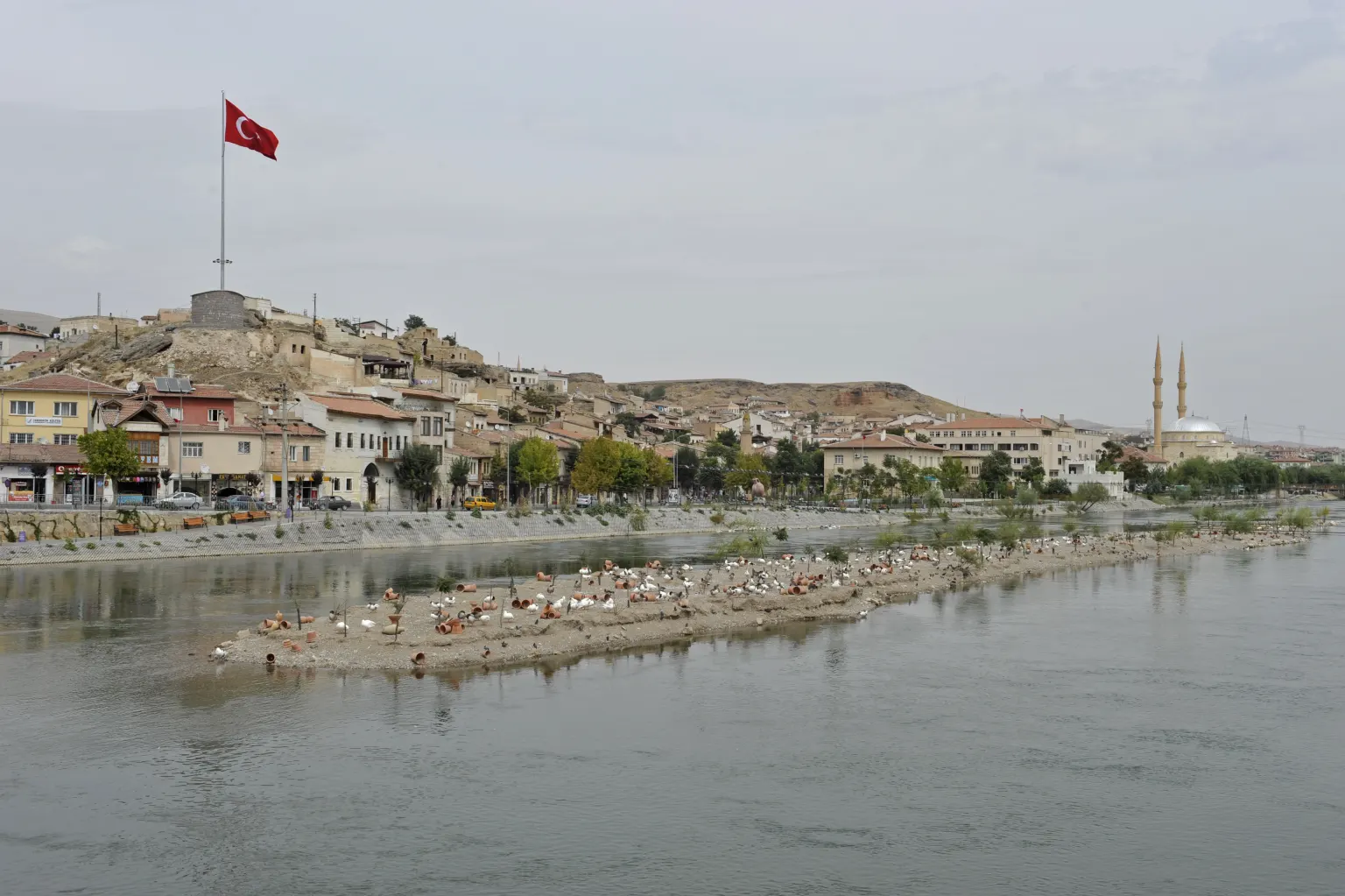 Un banc de sable dans le Kızılırmak avec des rangées de pots en terre séchant au soleil et des mouettes parmi eux, le fleuve à l’arrière-plan